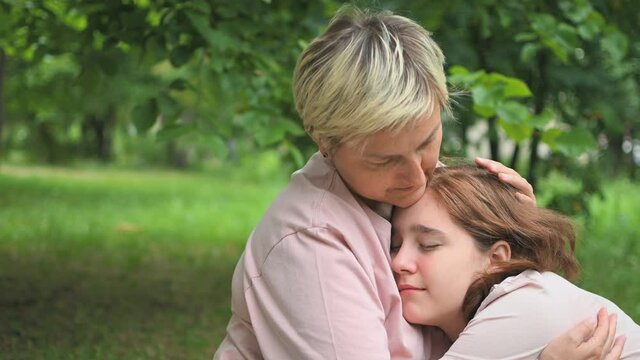 A mother calms her crying daughter sitting on a blanket in the park. Transitional age. First love.