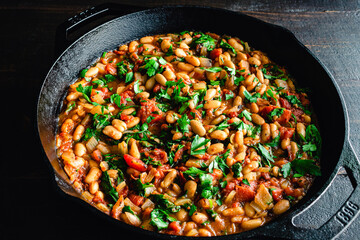 Vegan Spanish Beans with Tomatoes in a Cast Iron Skillet: Cannelinni beans, diced tomatoes, and spinach garnished with parsley in a cast-iron pan