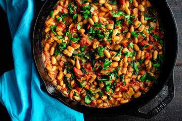 Vegan Spanish Beans with Tomatoes in a Cast Iron Skillet: Cannelinni beans, diced tomatoes, and spinach garnished with parsley in a cast-iron pan