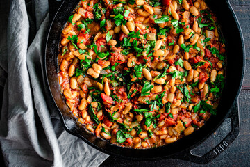 Vegan Spanish Beans with Tomatoes in a Cast Iron Skillet: Cannellini beans, diced tomatoes, and spinach garnished with parsley in a cast-iron pan