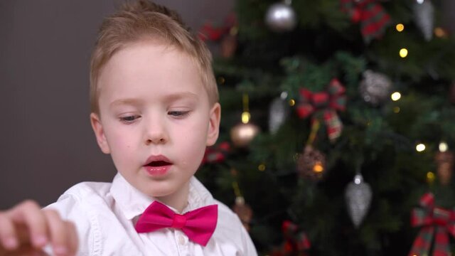 Portrait of naughty boy in white shirt with bow tie, eating candy who has been behaving badly all year so will not receive gifts from Santa for Christmas.