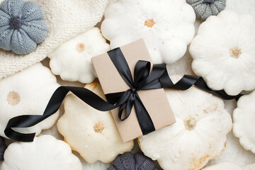 Stylish flat lay with uxury paper craft gift box and black satin ribbon bow on natural pumpkin squash background with copy space, discount, sale flyer, thanksgiving, harvesting monochrome concept