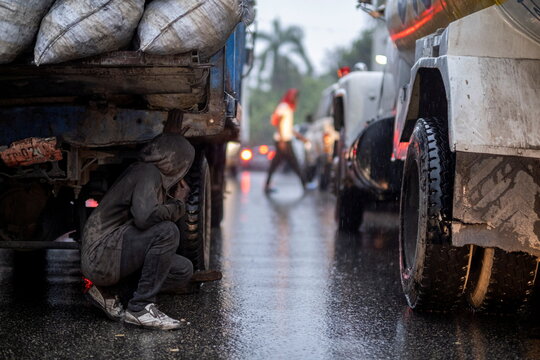 A man shelters from the rain under a cargo truck stuck in a traffic jam in Port-au-Prince