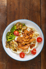 Udon with chicken in Japanese sauce and vegetables on a plate on a wooden table. Vertical photo