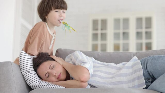 Tired upset single mother of hyperactive kid lying on sofa cover ears to avoid annoying noise from disobedient preschool son. Fatigued young mom exhausted disturbed with difficult child misbehavior