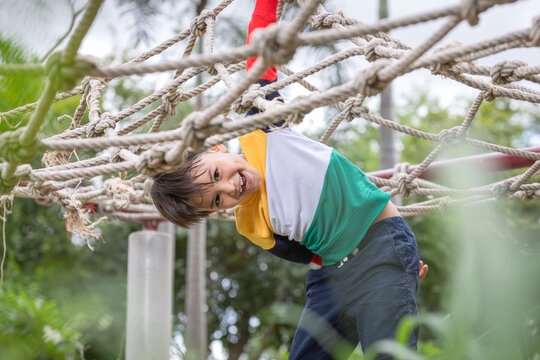 A boy wearing bright colored clothes climbing rope frame in the playground.The concept of healthy lifestyle.