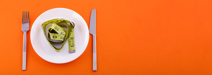 on a white plate lies a yellow measuring tape, a knife with a fork on an orange background. Weight loss and diet concept