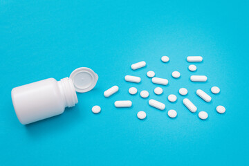 Global Pharmaceutical Industry and Medicinal Products - White Pills or Tablets Scattered from the Pill Container, Lying on Blue Background