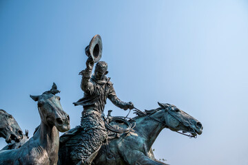 A statue of a cowboy riding his horse and tipping his hat stands out in the sun at the Calgary Stampede grounds.