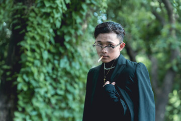 A young brooding asian man smoking a cigarette outside.