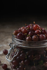 Ripe gooseberry berries of burgundy color close-up in a glass jar on a dark background. Dark and Moody, vertical orientation, copy space, no people