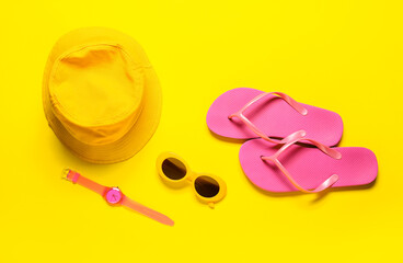Stylish sunglasses, hat, wrist watch and flip-flops on color background