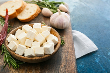 Bowl with delicious pieces of feta cheese on color background