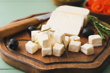 Board with delicious pieces of feta cheese on color wooden background