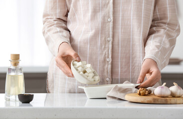 Woman holding bowl with pieces of feta cheese in kitchen