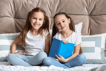 Cute little sisters reading book in bedroom
