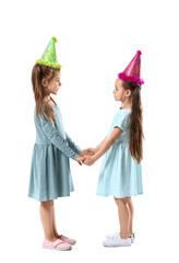 Cute little sisters in party hats on white background