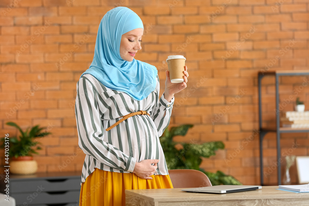 Wall mural Pregnant Muslim woman with cup of coffee at home