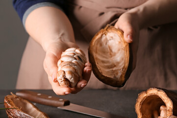 Woman holding fresh cocoa fruit at table, closeup