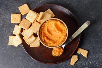 Bowl with tasty carrot hummus and crackers on dark background