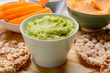 Bowl with tasty green pea hummus and rice crackers on table, closeup