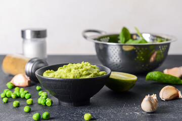 Bowl with tasty green pea hummus, lime and garlic on dark table, closeup