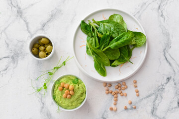 Bowl with tasty green pea hummus, olives and spinach on light background