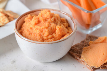 Bowl with tasty carrot hummus and crackers on light background, closeup