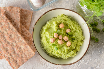 Bowl with tasty green pea hummus and crackers on light background, closeup