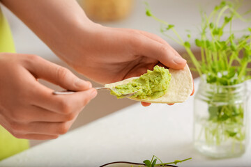 Woman spreading tasty green pea hummus onto pita on light background, closeup