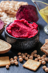 Bowl with tasty beet hummus, chickpeas and crackers on dark background, closeup