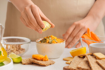 Woman squeezing lime onto tasty carrot hummus on light table, closeup
