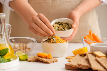 Woman preparing tasty carrot hummus on light table, closeup
