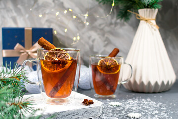 Warm medicinal winter tea in glass cups on the background of a pine branch. Christmas card. Two glass cups of tea with lemon and cinnamon sticks close-up on a Christmas background.