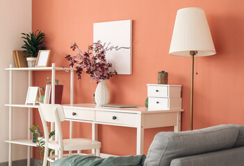 Modern workplace with vase and blossoming branches near color wall