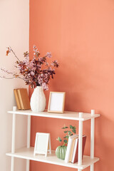 Book shelf and vase with blossoming branches near color wall