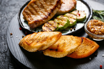 Board with tasty grilled bread and steaks on dark background