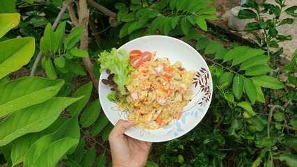 Omelet creamy with shrimps and crab stick with vegetables by hands on nature green leaf background.