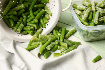Container and colander with frozen green beans on color wooden background