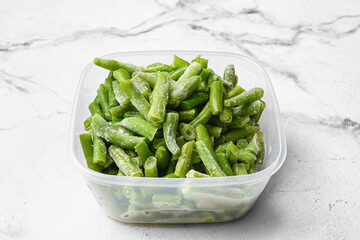 Container with frozen green beans on light background