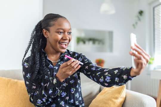 Happy, pregnant African woman is showing her pregnancy test and taking selfie making video call. Happy woman taking photo of pregnancy test with mobile phone and posting picture on social media.