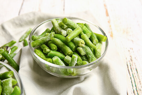 Bowl with frozen green beans on light wooden background