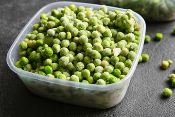 Container with frozen green peas on dark background