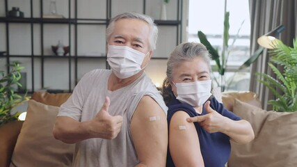 old asian senior couple wearing face mask virus protection happiness cheerful show bandage injection covid-19 vaccinated with hand gesture point and confident for virus protection - Powered by Adobe