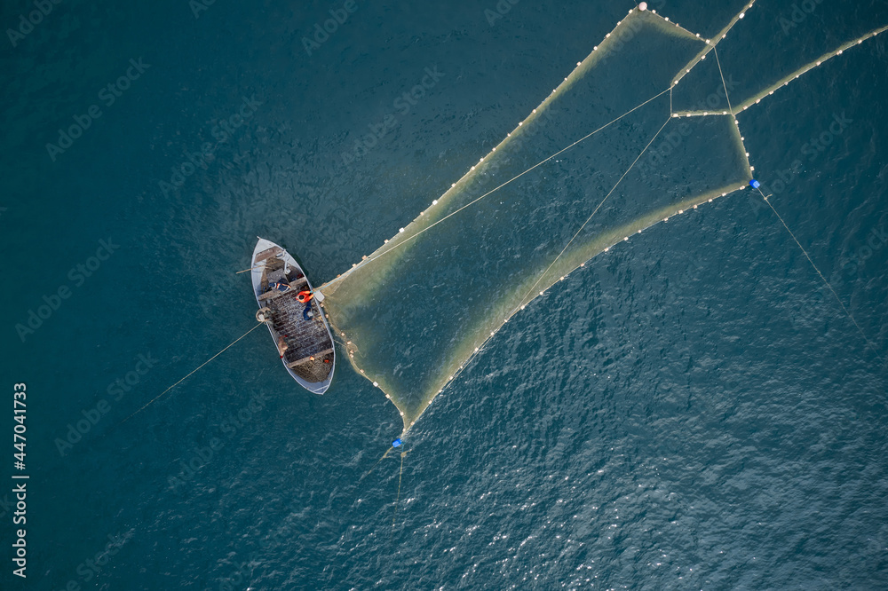 Wall mural Vintage wooden boat in coral sea. Boat drone photo. A fisherman on a fishing boat is casting a net for catching fish