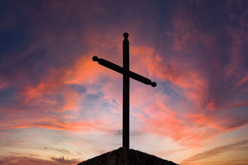 Antico crocifisso di metallo, con sfondo il cielo nuvoloso colorato al tramonto.
