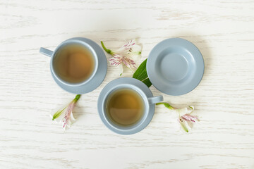 Cups of floral tea and flowers on light wooden background