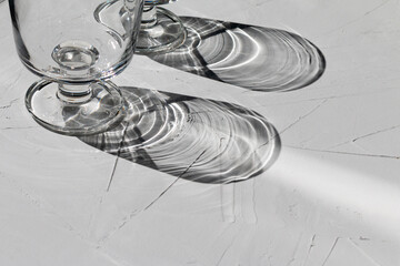 Glass on a grey concrete table with sunbeams and reflections, view from above, abstract shadows and sunlight
