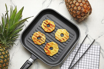 Frying pan with grilled pineapple slices on light background