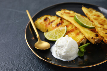 Plate with grilled pineapple slices and ice cream on dark background, closeup